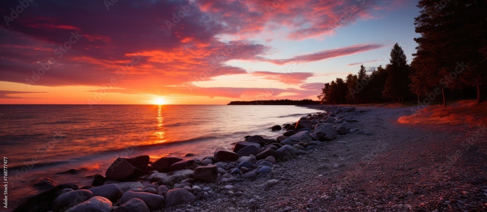 Aufkleber Tranquil sunset at the beach where a river flows into the sea, adorned with rocks and trees along the shore creating a peaceful scene