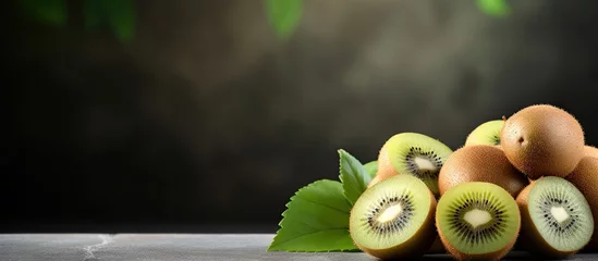 Poster A collection of ripe kiwi fruits displayed on a table, including whole fruits with green leaves and freshly cut slices on a slate board © vxnaghiyev