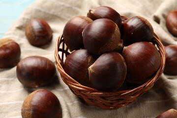 Wicker bowl with roasted edible sweet chestnuts on table, closeup