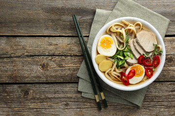 Delicious ramen in bowl and chopsticks on wooden table, flat lay with space for text. Noodle soup
