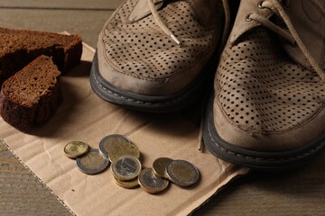 Poverty. Old shoes, coins, pieces of bread and cardboard sheet on wooden table, closeup
