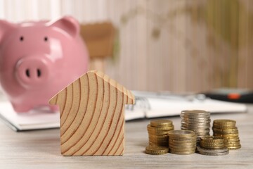 House model, stacked coins, piggy bank and notebook on wooden table, selective focus