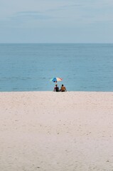 two people with umbrellas sit on a beach near the ocean