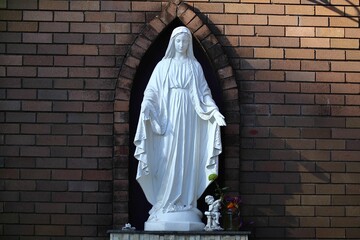 Majestic statue of the Virgin Mary is situated in a peaceful outdoor setting - obrazy, fototapety, plakaty