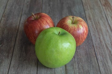 Two red and one green apple on a wooden table