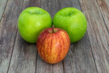 Apples on a wooden table - two green and one red