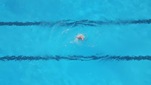A female athlete performs synchronized swimming routines in an outdoor pool, as seen from the air