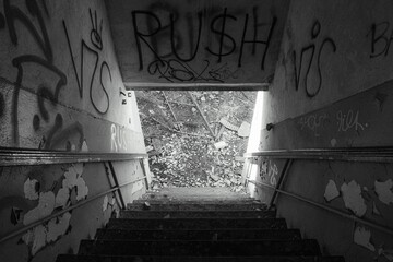 Greyscale of a stairwell in a dilapidated building, showing the graffiti artwork covering the walls