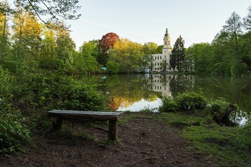 Quaint wooden bench sits peacefully alongside a tranquil river with a view of the Dammsmuhle Castle