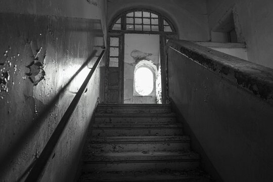 Aged building with a shadowy set of steps leading up to the entrance, greyscale
