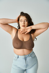attractive plus size young woman in brown bra and blue jeans looking to side and posing with hands - 768800095