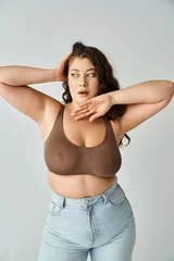 Poster attractive plus size young woman in brown bra and blue jeans looking to side and posing with hands © LIGHTFIELD STUDIOS