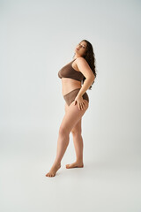 pretty plus size woman in underwear with hands on hips putting foot forward on grey background