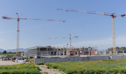 construction site in progress with hoist cranes and workers at work
