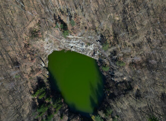 mining in the quarry has long since ended and the quarry is already reclaimed and blends into the forest landscape. circular deep flooded lake. search for the drowned using a police drone - obrazy, fototapety, plakaty