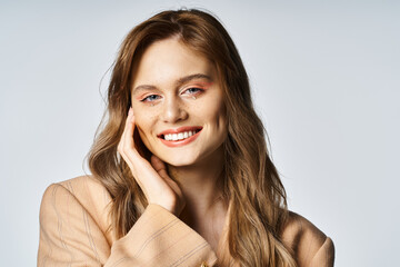 Attractive woman in beige jacket with tear shaped face jewels on grey background, peach fuzz