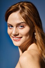 Fototapeta premium Side view shot of smiling girl with blue eyes, peach nude makeup with freckles on blue background