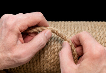 Jute rope close-up in a man's hand on a black isolated background. Environmentally friendly Material for creativity. Made from the Corchorus capsularis plant. Scratching post for cats.