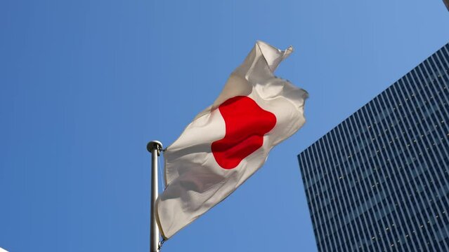 Low angle of a Japan flag waving under a modern skyscraper and blue sky