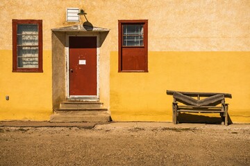 Weathered wooden bench sits alone outside a red-painted door, seemingly forgotten.