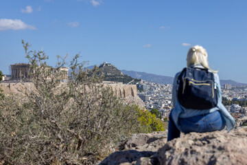 Blonde woman on Mouseion Hill observing beautiful view of Acropolis of Athens and Mount Lycabettus,...