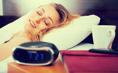 Woman sleeping near clock and book in bedroom