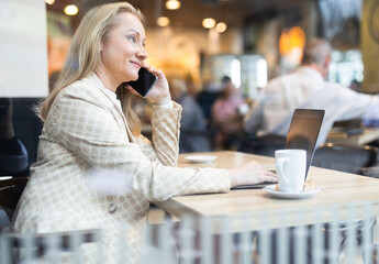 Businesswoman sitting at cafe table and talking on mobile phone