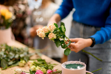 Female hands of the florist hold one sprig of rose with four buds over the table