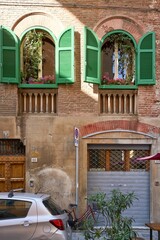 Green shutters with flowers in an old historic brick building Pisa, Tuscany, Italy.