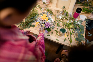 Female florist's hands finish arranging a bouquet of colorful roses and wildflowers on a table