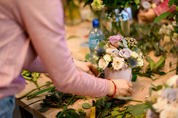 Female florist's hands hold a small bouquet of colorful roses and wildflowers