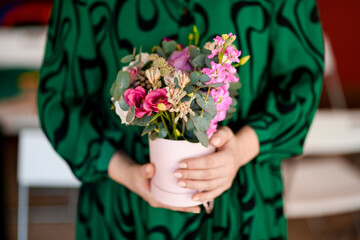 Female hands of a florist in a green dress hold a delicate bouquet of various flowers