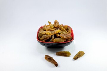 Close-up of a red bowl filled with dried raisins against a white background