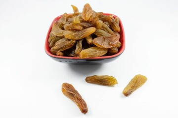 Close-up of a red bowl filled with dried raisins against a white background