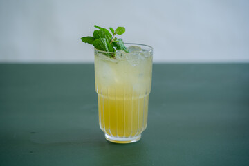 Fresh Coctail with Yellow Color and Mint Leaf as Garnish on top of the Glass.