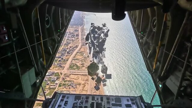 PALESTINE - 3.12.2024 - Parachutes carry airdrop supplies down from a USAF aircraft to a coastal area of Palestine.
