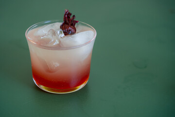 Coctail Drink with Red Color in a small Glass with Rosella Flower on top as Garnish