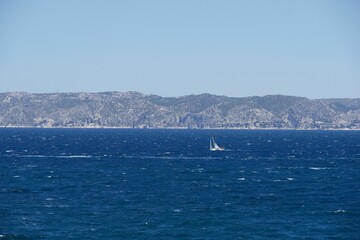 Sailboat gliding across a sparkling blue sea with mountains and a blue sky in the background