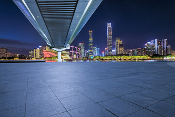 Empty square floor and pedestrian bridge with modern city buildings at night