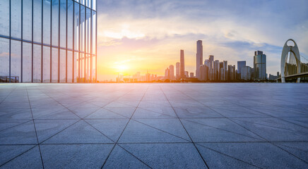 Empty square floor and glass wall with modern city buildings at sunset in Guangzhou. Panoramic view.