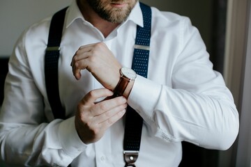 Closeup shot of a groom adjusting a wristwatch on his arm. - obrazy, fototapety, plakaty