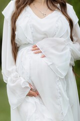 Glowing pregnant woman wearing a pristine white dress posing holding her belly