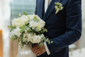 Handsome groom stands with a white bouquet in his hands