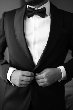 this is black and white photograph of a man in a suit fixing his buttons