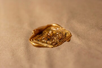 Closeup of a wax seal of the letter "L" on a beige fabric