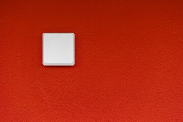 a red wall with a white square light switch on it
