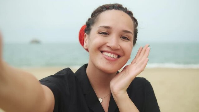 Young caucasian pretty woman with red dreadlocks making selfie with happy smile with ocean beach on background