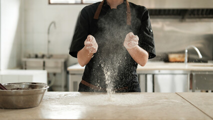 Close-up of the hands of a female pastry chef whose hands are covered in flour and she claps her...