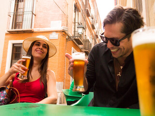 straight Hispanic Caucasian couple with sunglasses and dental braces she looks at him laughing drinking beer on a terrace of a Spanish bar - 768851452