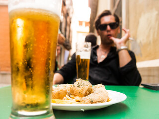 fried fish appetizer on the terrace of a bar with out of focus tourist with cigar and glasses and glass of beer on terrace of spanish bar in granada - 768852002